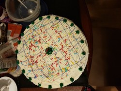 White cake with white frosting, purple cookie icing, sprinkles and green writing icing